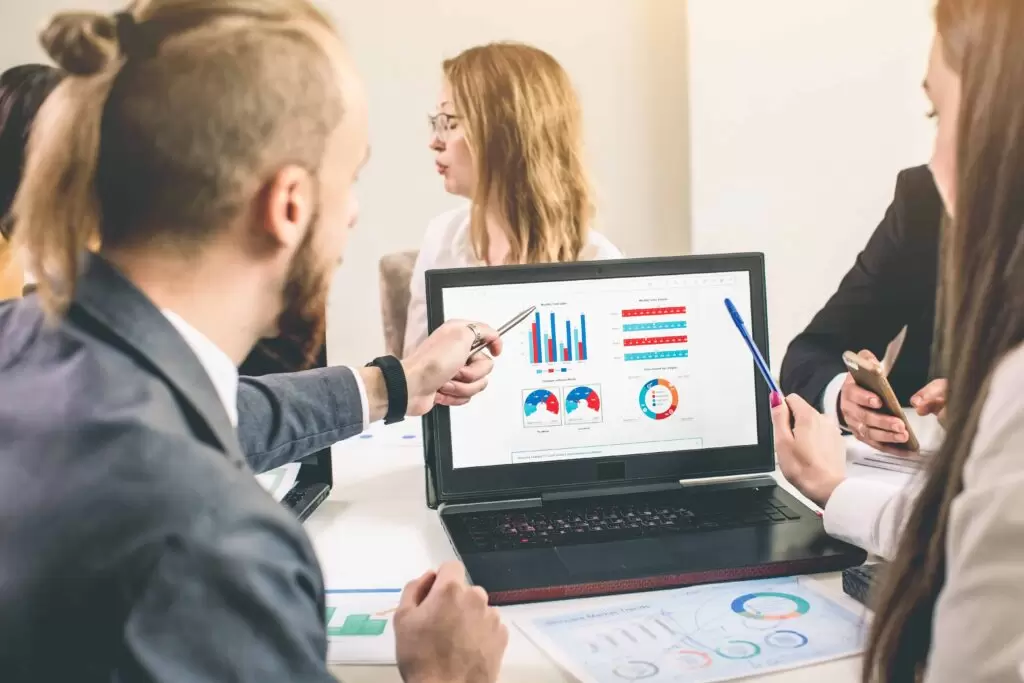 A team of business professionals collaborates on a laptop displaying data charts, discussing end-to-end claims processing and analytics. The scene highlights a data-driven approach to an efficient claims workflow.