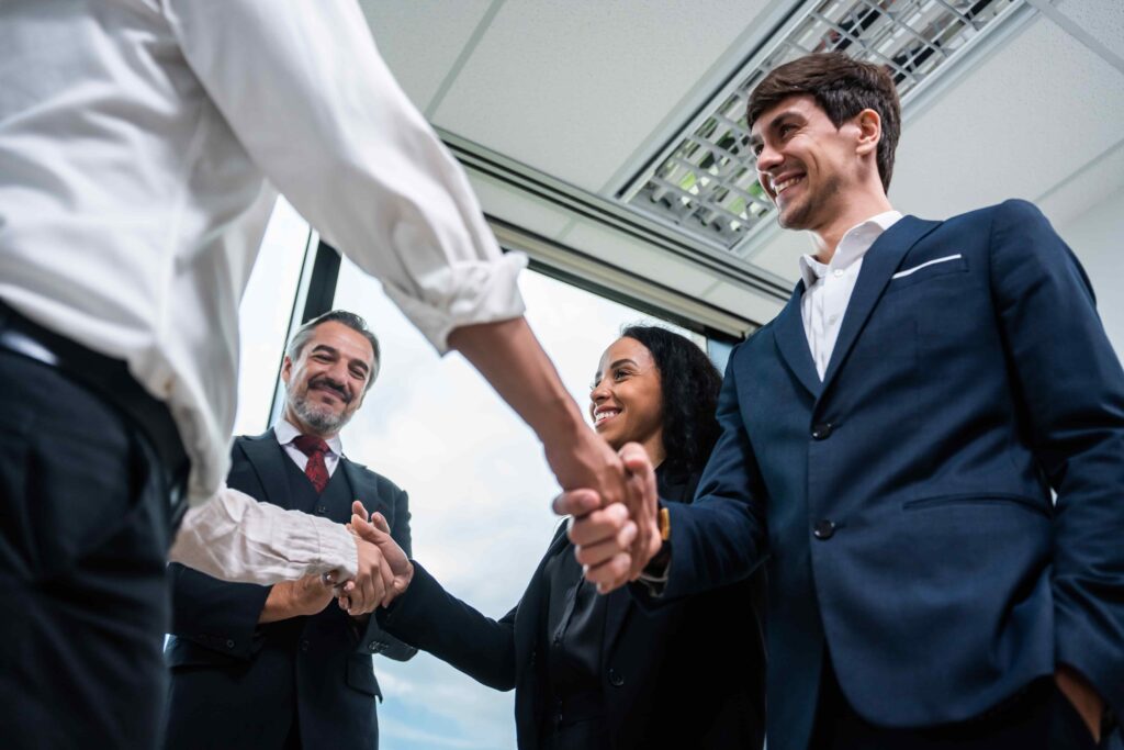 A diverse group of business professionals, including a Caucasian businessman and an African American businesswoman, smiling and shaking hands, representing successful collaboration in outsource underwriting services.