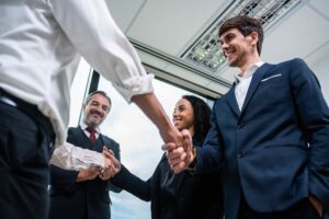 A diverse group of business professionals, including a Caucasian businessman and an African American businesswoman, smiling and shaking hands, representing successful collaboration in outsource underwriting services.