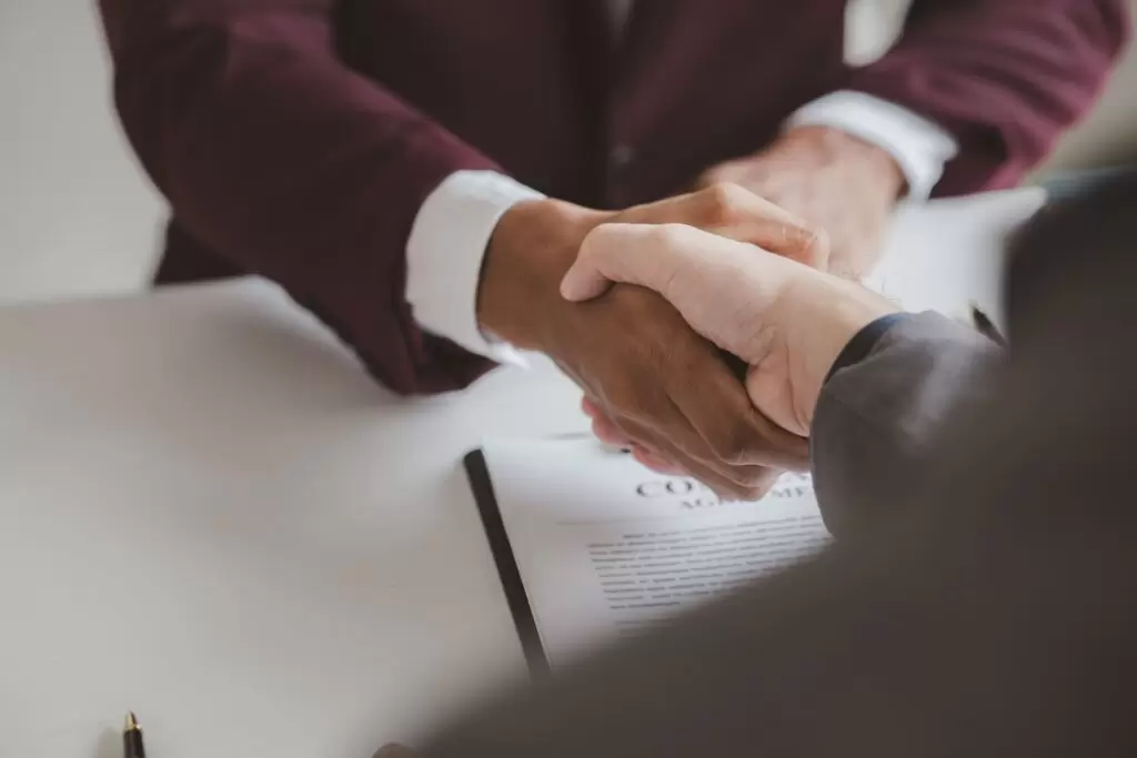 Close-up of two business people shaking hands over a contract, symbolizing a completed agreement for professional outsource underwriting services.